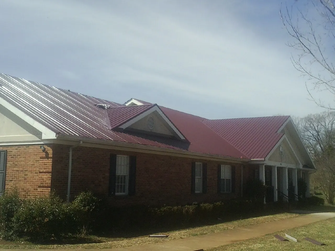 Red metal roof with gabled entries on a long brick building, from a Hail Damage Roof Repair job in Prosperity