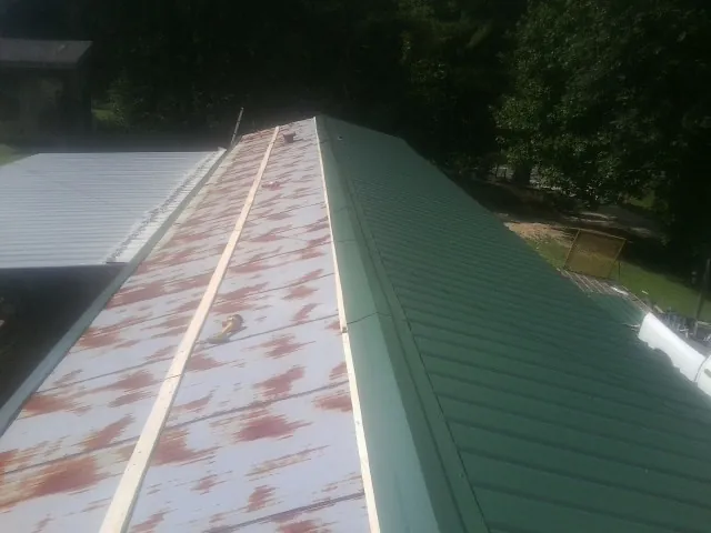 Old rusted panels beside newly installed green metal roofing — Wind Damage Roof Repair by Roofing Brothers in Prosperity