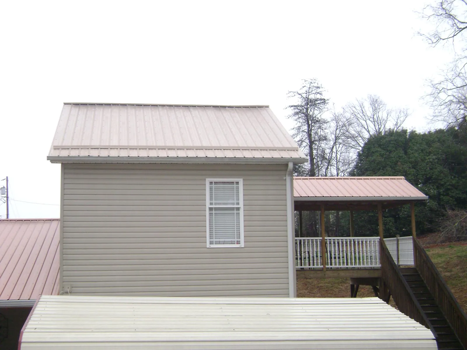 Tan metal roofs on a two story addition and attached porch, from a Roof Replacement job in Prosperity